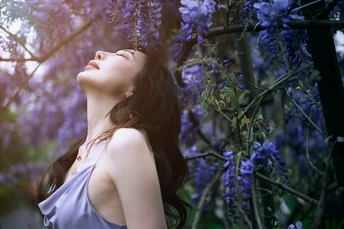 一位穿着蓝色连衣裙的美丽年轻女子站在紫花下