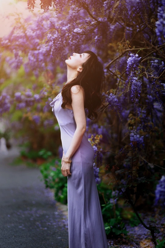 一位穿着蓝色连衣裙的美丽年轻女子站在紫花旁边