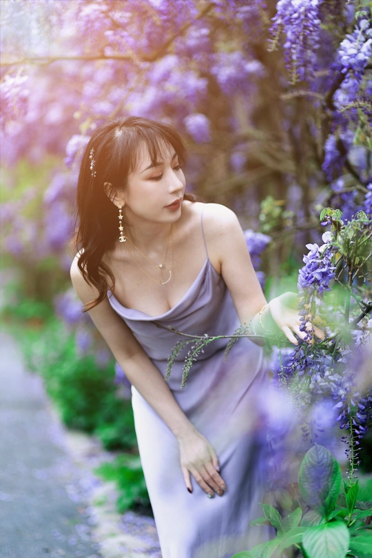 一位穿着蓝色连衣裙的美丽年轻女子沿着开满紫花的小径行走