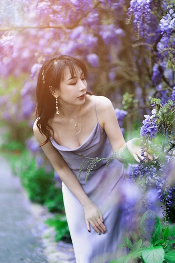 一位穿着蓝色连衣裙的美丽年轻女子沿着开满紫花的小径行走