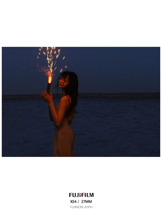 一个女人晚上站在海滩上 在水面前拿着一个闪闪发光的东西