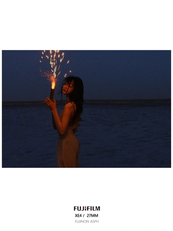 一个女人晚上站在海滩上 在水面前拿着一个闪闪发光的东西