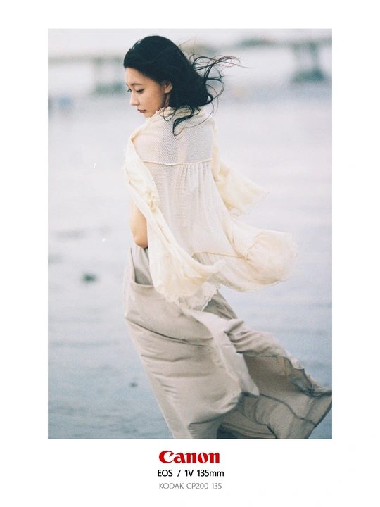 一个穿着白色连衣裙的年轻女子沿着海滩散步