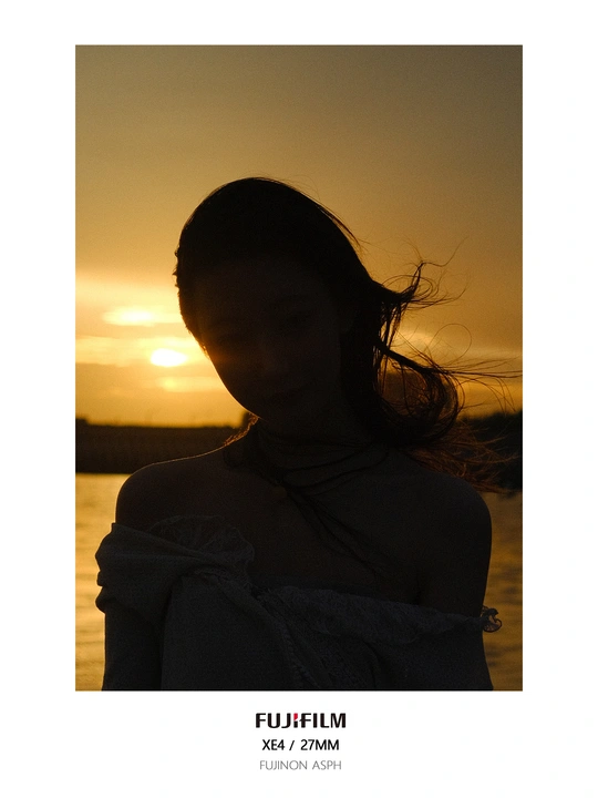 日落时 一位裹着包裹的年轻女子站在水体前的剪影