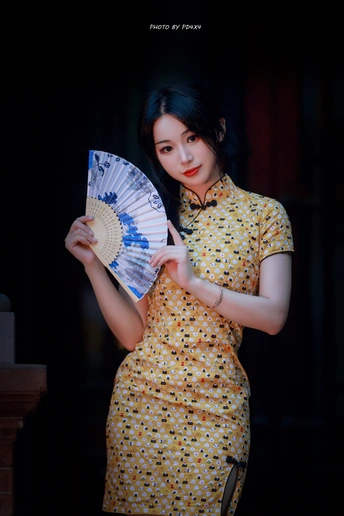 一位身穿黄色连衣裙的年轻女子手里拿着扇子和雨伞