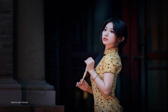 一位身穿黄色连衣裙、撑着雨伞的年轻女子站在一栋楼前