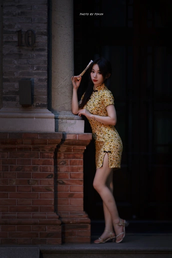 一个穿着黄色连衣裙的年轻女子靠在砖墙上 手里拿着棒球棍和雨伞