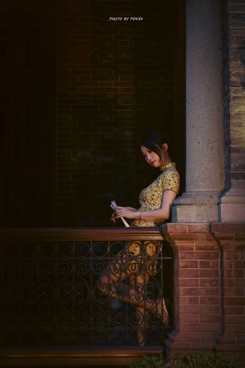 一名身穿黄色连衣裙的年轻女子晚上坐在一栋楼的阳台上看手机