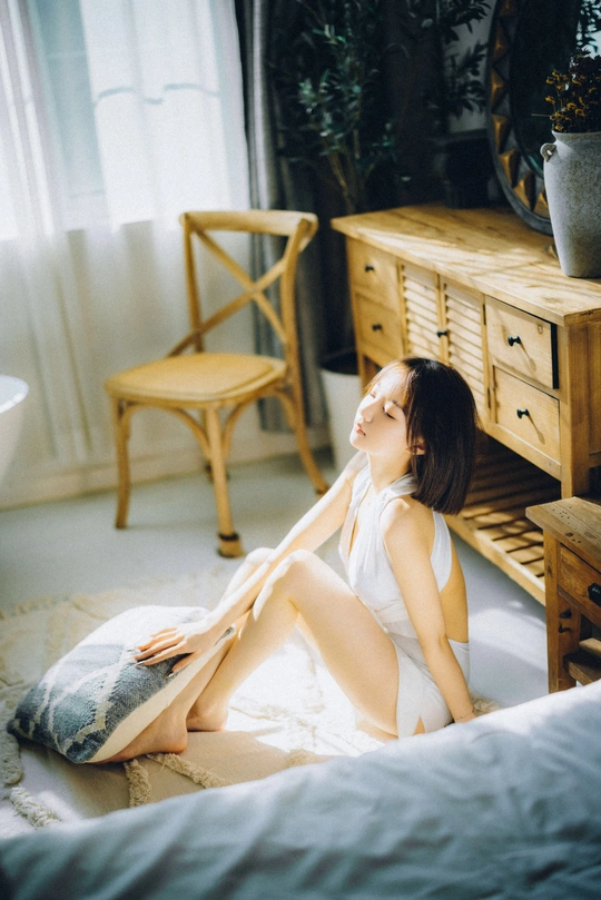 一个年轻女子坐在一张床边的一间白色房间里 有一把椅子。