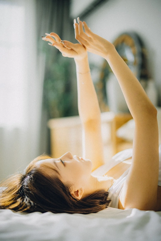 一个年轻女子躺在床上 手臂伸直 双手举过头顶