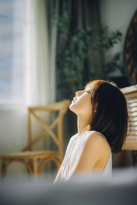 一个年轻女子坐在钢琴前面的长椅上 面对窗户 太阳紧挨着她。