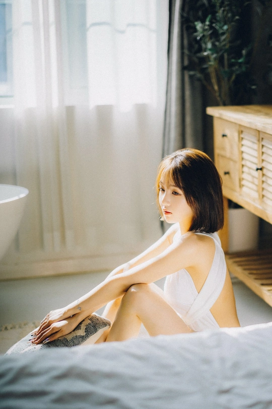 一个年轻女子坐在浴室的床上 披着一条白毛巾。