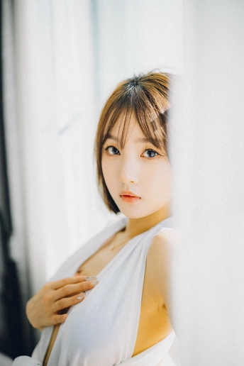 一位穿着白色连衣裙的年轻女子站在窗户前