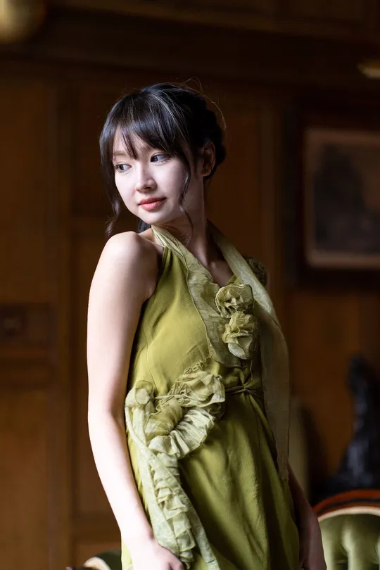 一位穿着绿色连衣裙的年轻女子站在一个古董客厅里