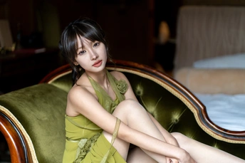 一个穿着黄色连衣裙的年轻女子坐在绿色沙发上 双腿交叉穿着一件短白色连衣裙。