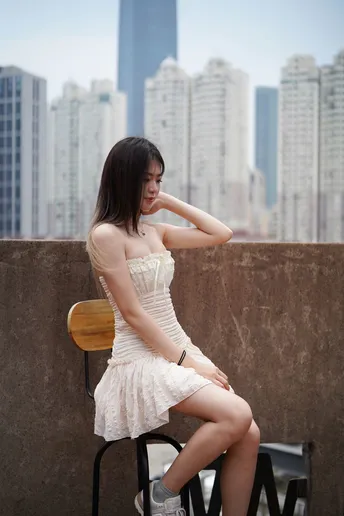 一个穿着白色连衣裙的年轻女子坐在阳台上 俯瞰着城市的轮廓线。