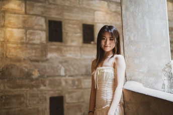 一位穿着漂亮裙子的年轻女子站在有柱子的墙边 旁边有一扇窗户。