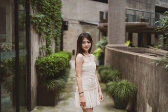一个美丽的年轻女子穿着白色连衣裙站在建筑物之间的巷子里