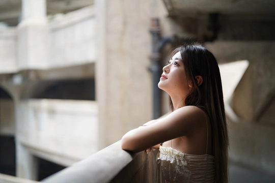一位穿着美丽裙子的年轻女子倚靠在围栏上 凝视着一座建筑物的窗户。