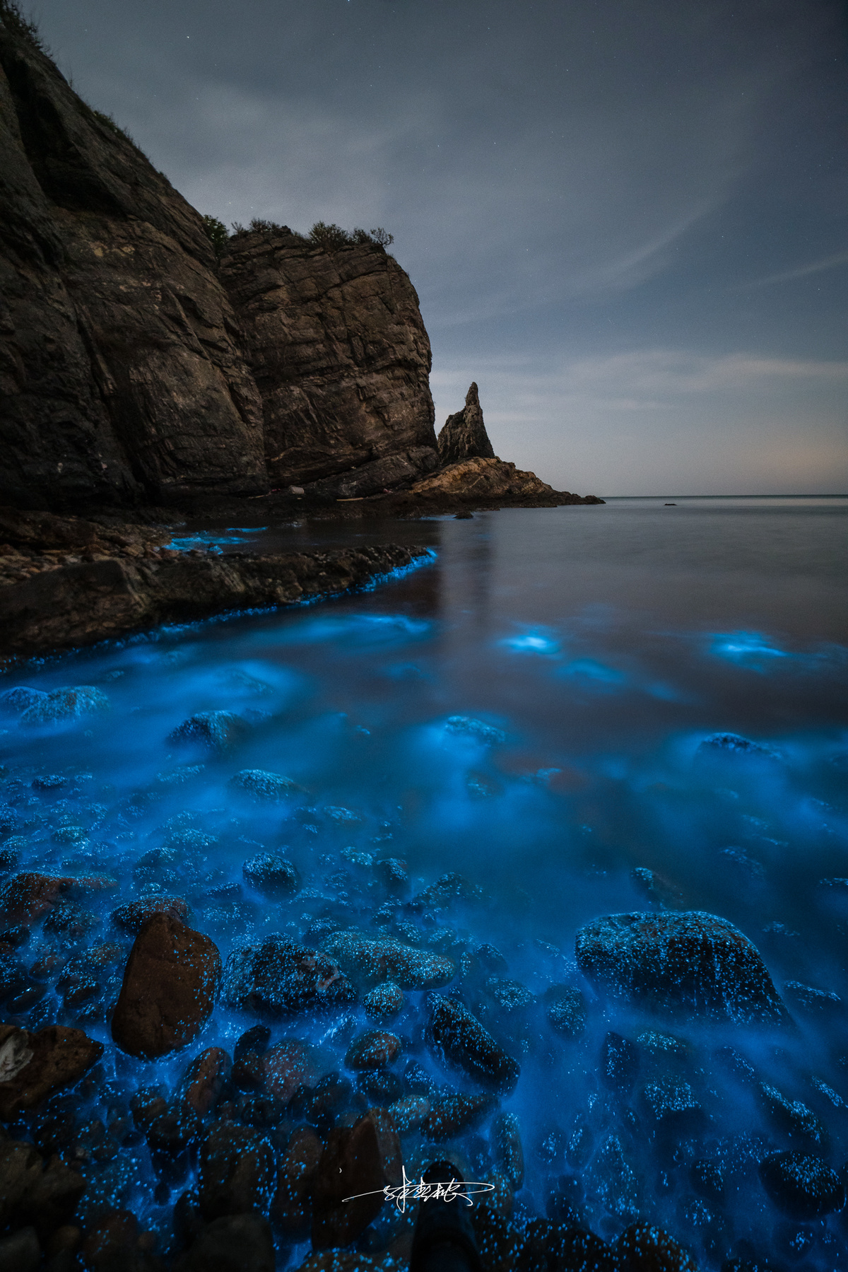 夜晚被蓝色光芒照亮的岩石海滩 前景中有一片水域。