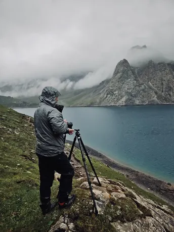 一个人正在用三脚架相机拍摄湖泊和山脉作为背景的照片。