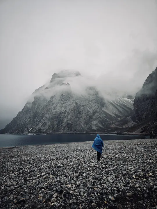 一个男人站在砾石路上 背景是湖和山。