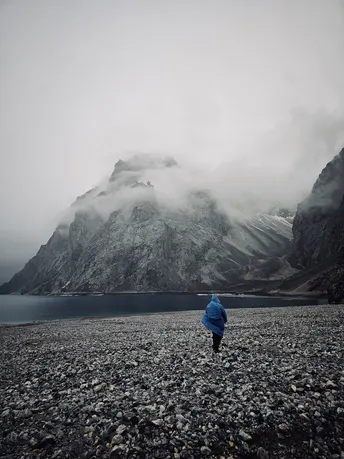 一个男人站在砾石路上 背景是湖和山。