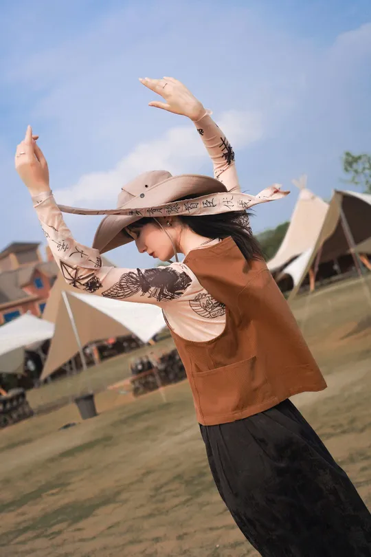 一位戴着牛仔帽的女人站在田野中 双臂伸展向天空。