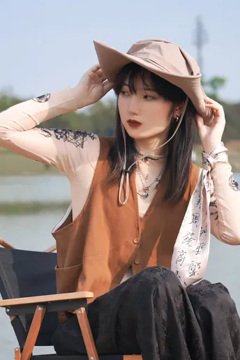 一位戴帽子坐在河边椅子上的女士