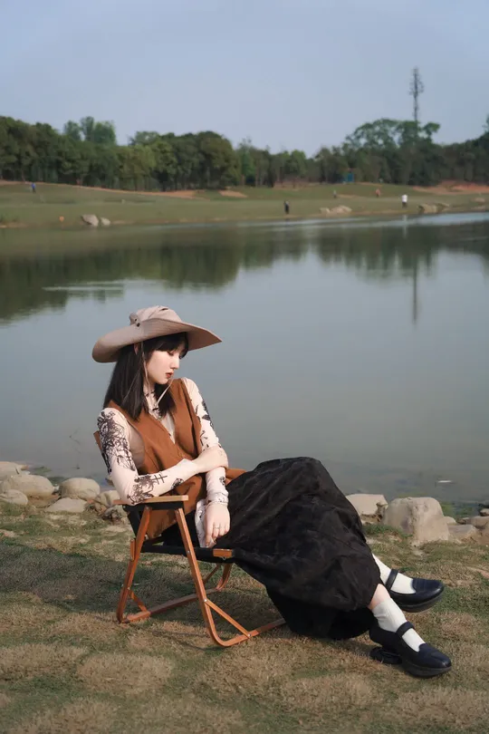 一位戴帽子的女士坐在湖边或水边的椅子上