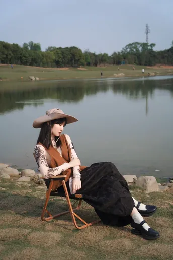 一位戴帽子的女士坐在湖边或水边的椅子上