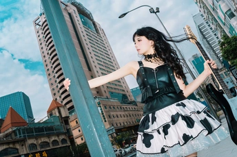 一位穿着黑白裙子的年轻女子站在一根柱子旁边 手里拿着一把伞。