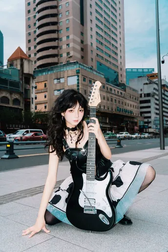 一个穿着连衣裙的女人坐在人行道上 带着一把吉他 在城市中。