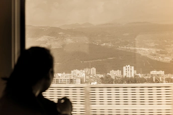 一位女性坐在窗前 凝视着远方山脉中的城市轮廓。