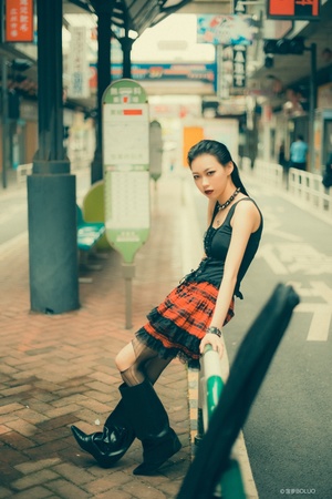 一名穿着黑色连衣裙和靴子的年轻女子在火车站附近街道上摆姿势