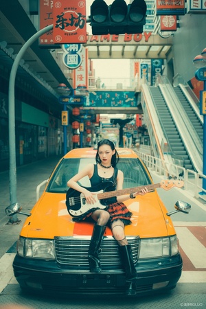 一个年轻女子坐在橙色出租车的车盖上弹吉他