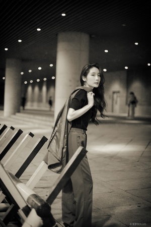 一张黑白照片 一位年轻女子正在她的行李旁边的一张长凳上站着。