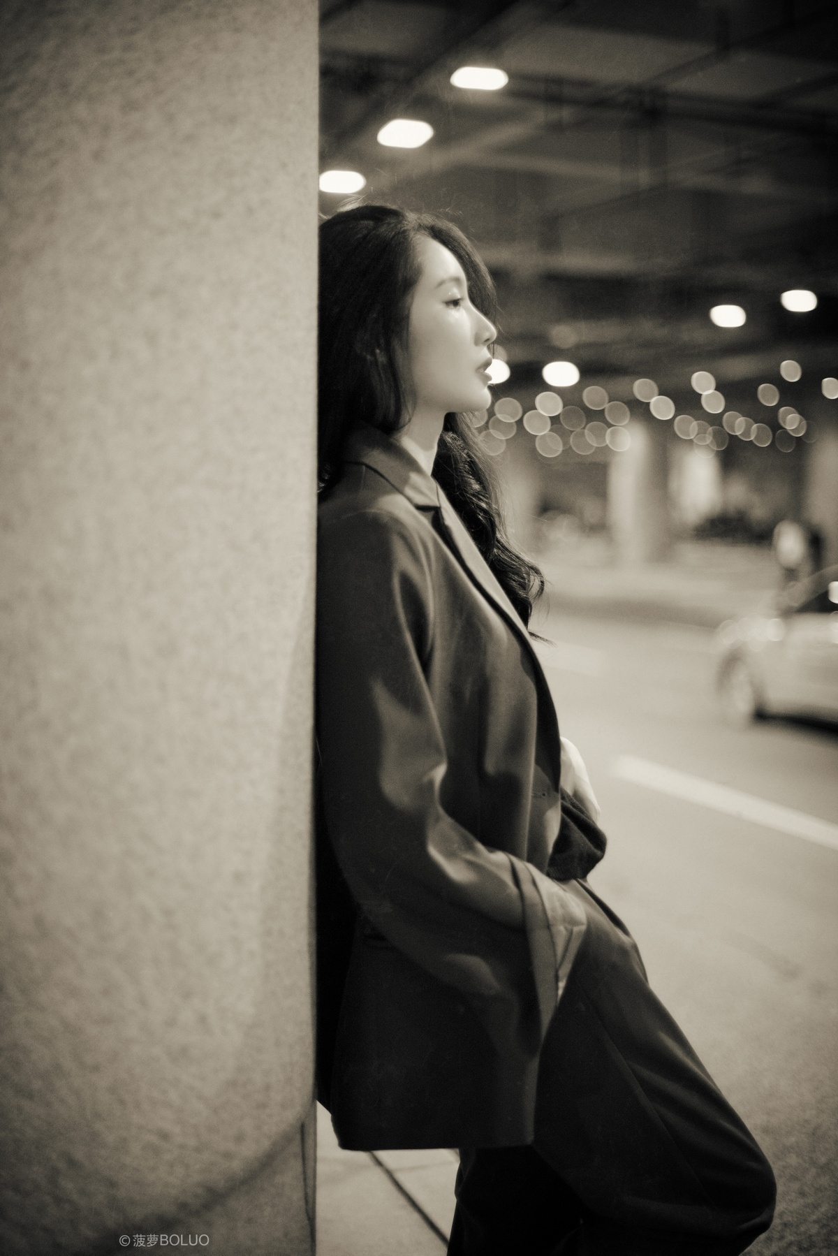一位年轻女子靠在墙上 黑白色调 看着街道。