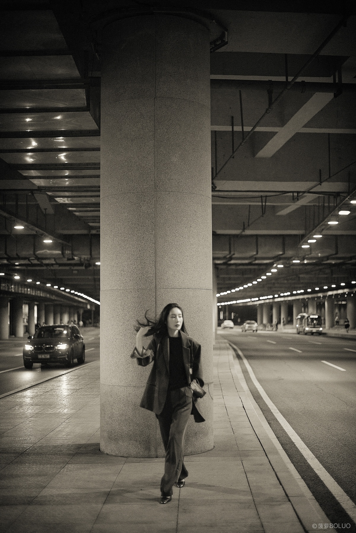 一张黑白照片 一位女子正在人行道上靠着一根柱子走动。