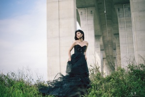 一个穿着黑色长袍的美女站在桥下草地中