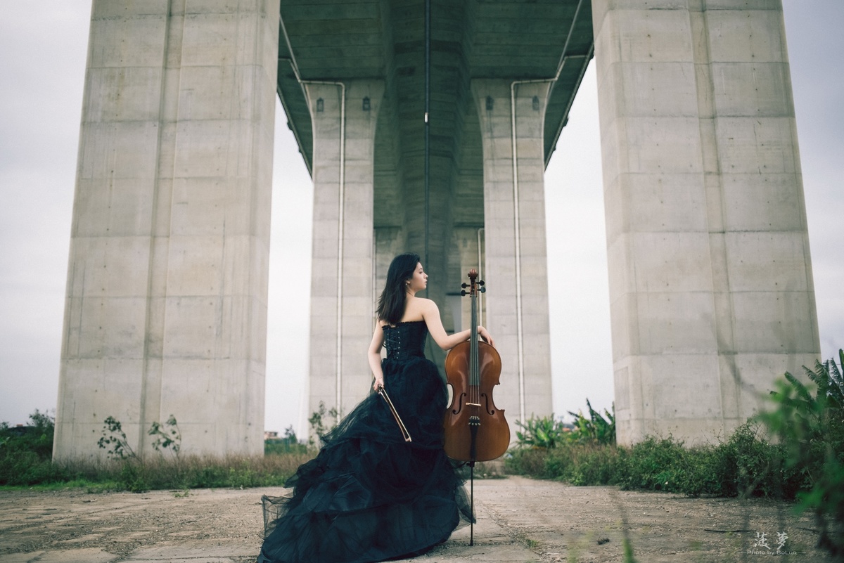 一个穿黑色连衣裙的女人在桥下演奏小提琴