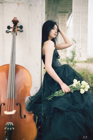 一个穿着黑色长袍的年轻女子坐在小提琴和白色花旁边