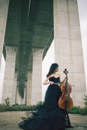 一个穿着黑色连衣裙的年轻女子站在桥下 拿着一把小提琴。