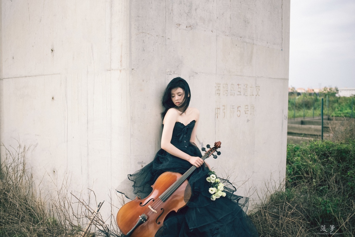 一个穿黑色连衣裙的年轻女子坐在混凝土墙上弹奏小提琴