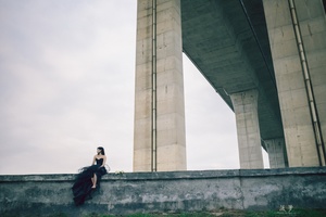 一张女性穿着黑色连衣裙坐在桥下墙上的照片