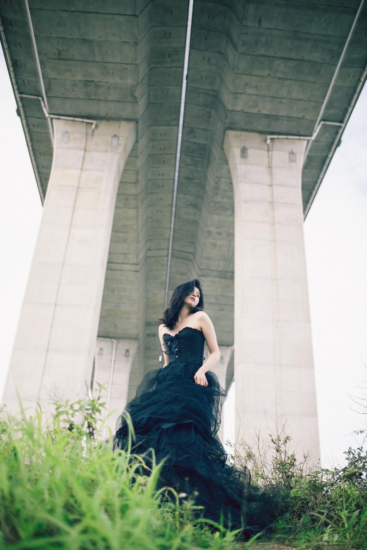 一个穿黑色连衣裙的女人站在桥下
