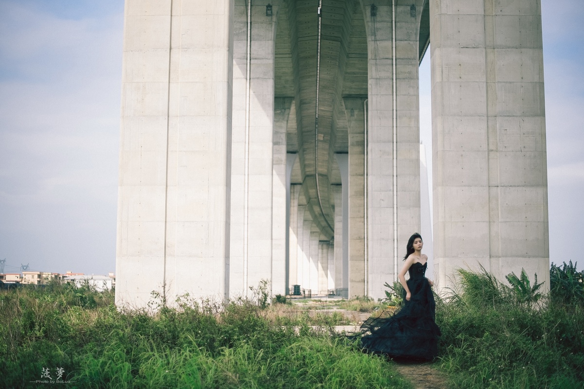 一个穿黑色连衣裙的女人站在桥下