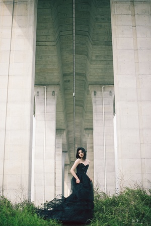 一位穿着黑色连衣裙的女子站在桥下草地