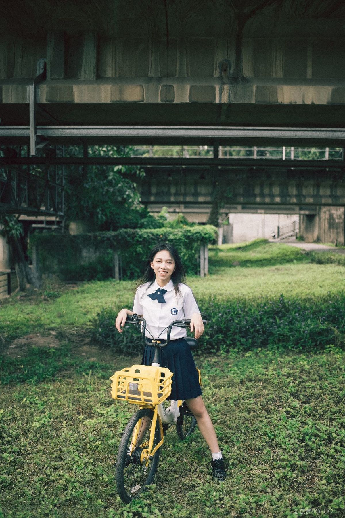 一位年轻女子站在田野中 手里拿着一辆带篮子的黄色自行车。