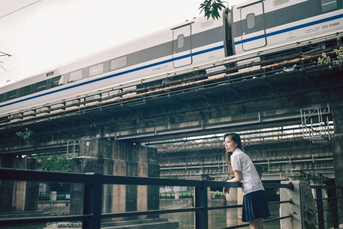 一个站在桥上 火车从水面经过的女人带着一个手提箱。